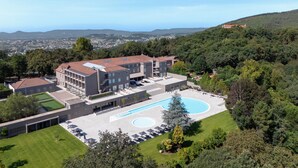Un hotel moderno con piscina, rodeado de vegetación exuberante y colinas al fondo.