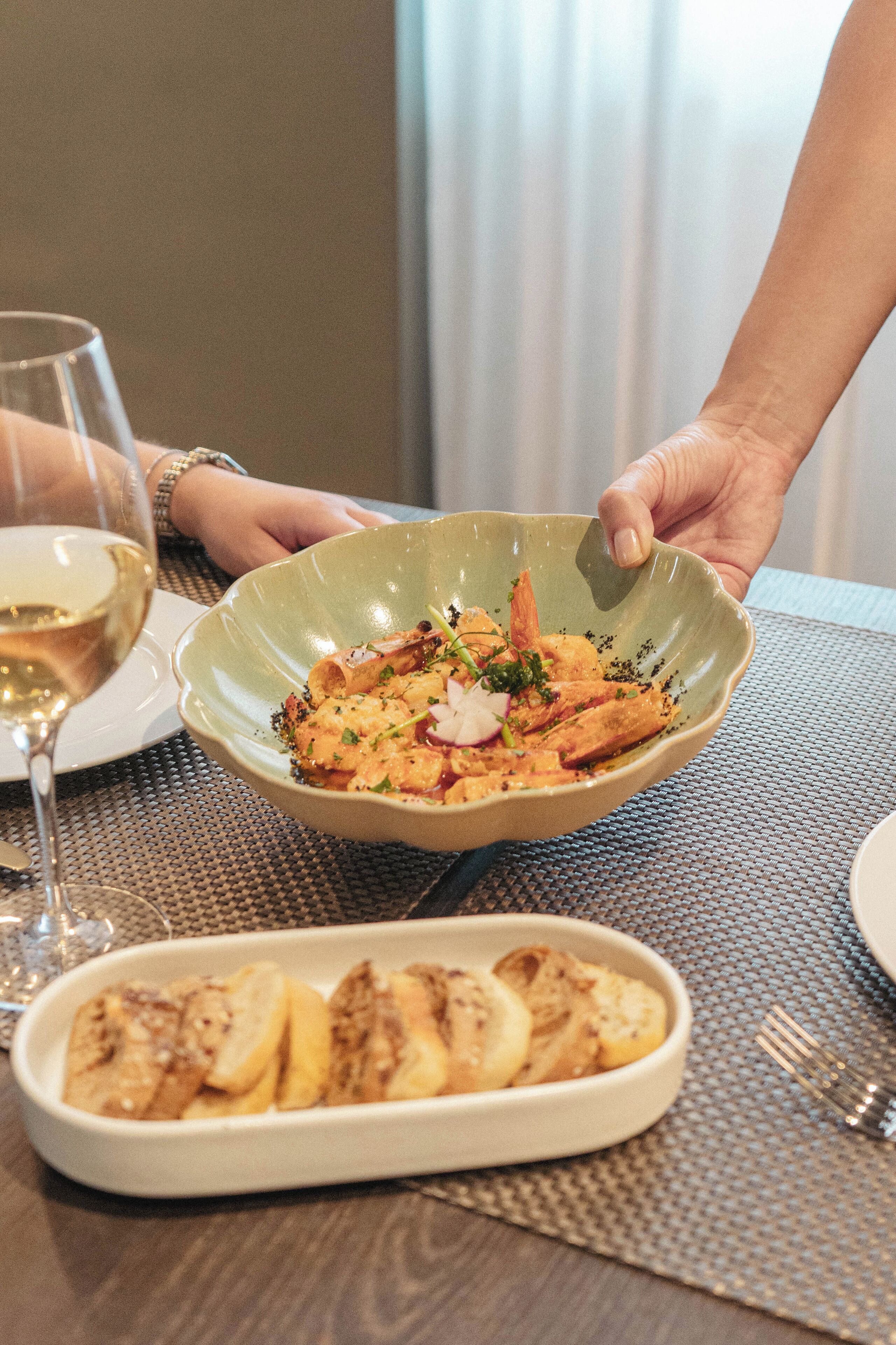 A dining table with a plate of food, a glass of white wine, and a fork.