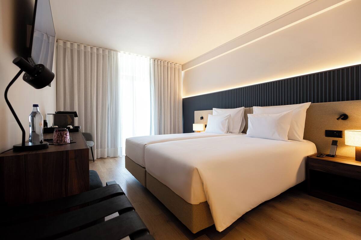 Een moderne hotelkamer met een groot bed, nachtkastjes, een bureau met lamp en een aan de muur bevestigde televisie.