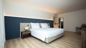 Ein modernes Hotelzimmer mit einem großen Bett, einem Nachttisch mit Lampe, Holzboden und einer dunkelblauen Akzentwand.