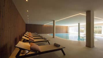 A modern indoor pool area with sun loungers and a clear view of the pool.