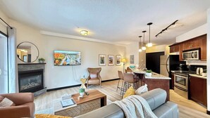 A modern living room with a fireplace, a sofa, a coffee table, and a TV mounted on the wall. - Grande Rockies - Newly Renovated MTN View Retreat (Canmore)