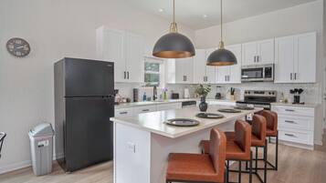 Una cocina moderna con gabinetes blancos, un refrigerador negro, una isla central con taburetes altos e iluminación colgante.