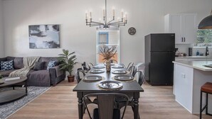 A modern kitchen with a dining table set for six, a black refrigerator, and a pendant light above the table.