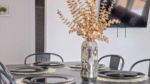 A dining table with a vase of dried flowers, black plates, and a flat-screen TV mounted on the wall.