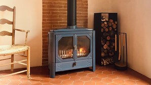 A corner room with a wood-burning stove, a chair, and a log display. - Renovated barn, quiet gîte- Céret (Vivès)
