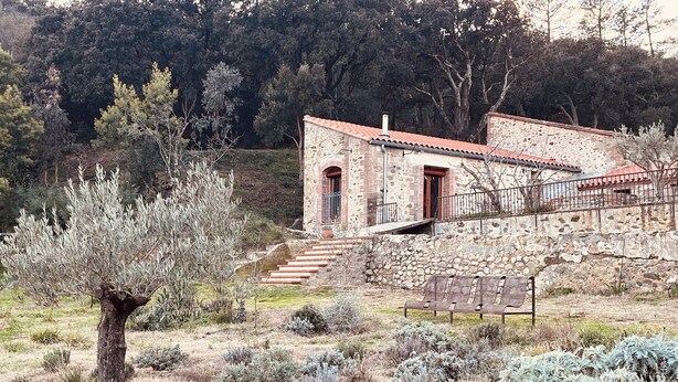A stone building with a red-tiled roof, a staircase leading to a door, and a bench in the foreground. - Renovated barn, quiet gîte- Céret (Vivès)