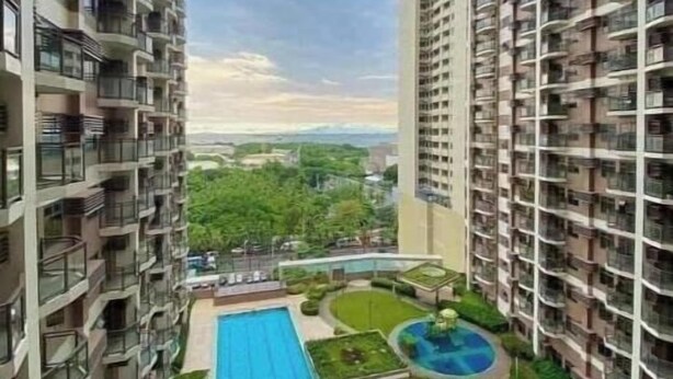 Un immeuble résidentiel de grande hauteur doté de nombreux balcons, d’une piscine centrale et entouré de verdure.