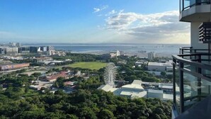 Un edificio alto con balcón de vidrio que ofrece vistas a una ciudad costera, incluyendo una noria y varios edificios.