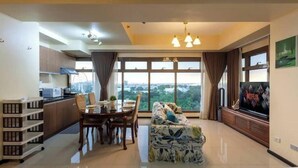 A modern living room with a dining area, large windows, and a flat-screen TV. - 10G The Sunset Executive @ The Radiance Manila Bay (Pasay City)