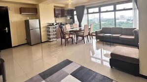 A spacious living area with a dining table, sofa, and a view of the city through large windows. - 10G The Sunset Executive @ The Radiance Manila Bay (Pasay City)