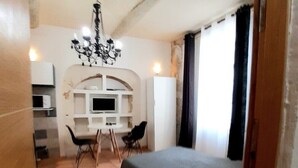 A small, compact room with a bed, a desk, and a chair. There is a chandelier hanging from the ceiling, and a window with curtains. - Historic center apartment close to the lively and dynamic hyper center. (Unknown)