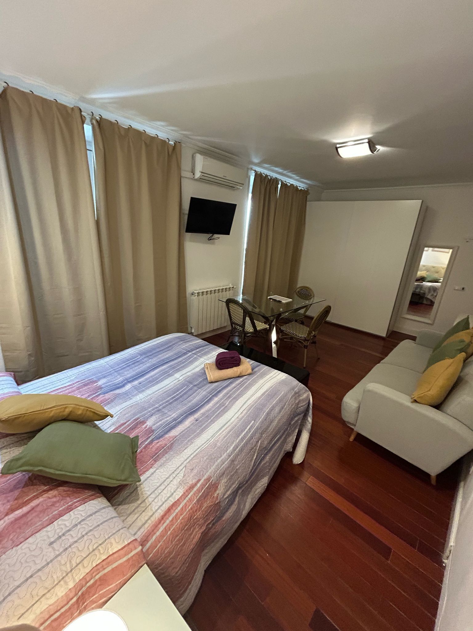 A hotel room with a bed, a sofa, a TV, and a dining area.