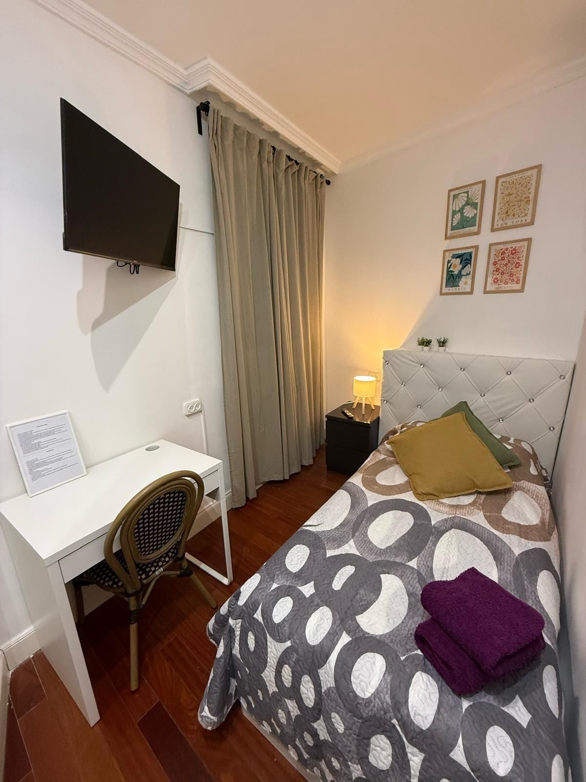 Een hotelkamer met een bed, bureau, stoel, televisie, nachtkastje en een lamp.