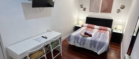 Habitación de hotel pequeña con cama, escritorio, televisor y radiador.