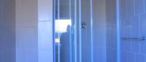 A modern bathroom with a glass-enclosed shower, white tiled walls, and a visible trash bin.