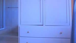 Een witte kast met twee lades en twee deuren, een rookvrij bord aan de muur, en een blauw gordijn dat deels zichtbaar is.