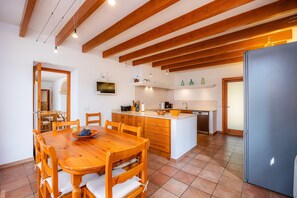 Een ruime keuken met houten balken, een eettafel met stoelen, een koelkast en een spoelbak.