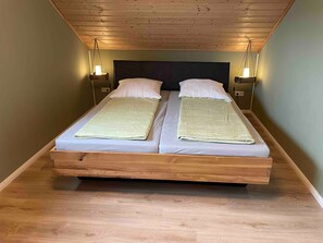 Un lit double avec un cadre en bois, deux tables de chevet avec des lampes et un plafond en pente.
