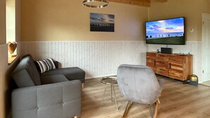 Ein modernes Wohnzimmer mit Sofa, Sessel, Fernseher und Holzschrank.