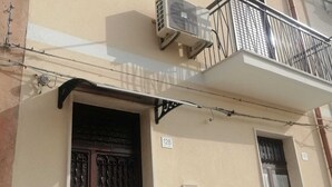 A building with a beige facade, a dark wooden door, and a balcony with a metal railing. - Long Term Vacation Home (Noto)