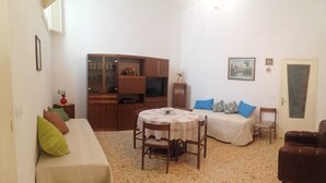 A small, cozy room with a bed, a sofa, a dining table, and a cabinet. - Long Term Vacation Home (Noto)