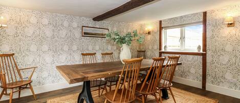A dining room with a wooden table and chairs, a vase with greenery, and patterned wallpaper.