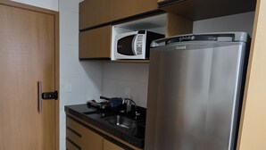 A compact kitchen with a stainless steel refrigerator, a microwave, and wooden cabinets.