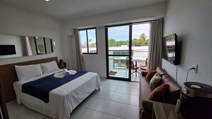 A hotel room with a bed, a sofa, a TV, and a balcony with outdoor furniture.