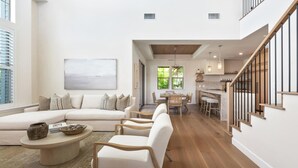 Un amplio espacio habitable con un sofá grande, dos sillones, una mesa de centro y una mesa de comedor. Una escalera con barandillas de madera conduce a un nivel superior.