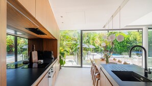 A modern kitchen with a large window, a black countertop, and wooden cabinets. - Villa Roche Blanche - Jardin tropical avec piscine (Marseille)