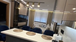 Cozinha moderna com ilha central, eletrodomésticos embutidos e área de refeições com cadeiras azuis.