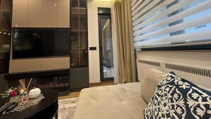 Uma sala de estar moderna com televisão de tela plana, armários embutidos, lareira e uma janela grande com persianas.