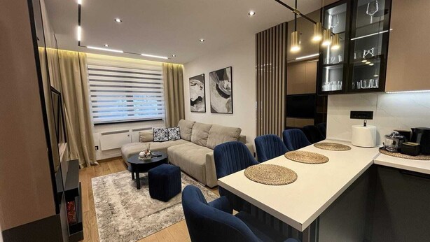 Uma sala de estar moderna com sofá, mesa de centro e cadeiras azuis. Há uma área de jantar com mesa e cadeiras, e uma cozinha com bancada e armários.