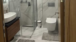 Casa de banho moderna com cabine de duche envidraçada, toucador com lavatório e sanita.
