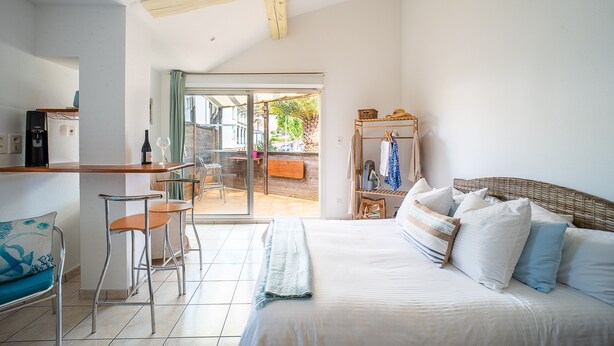 A bedroom with a bed, a chair, a small table, and a view of the outside. - Sable entre les Orteils - Studio vue mer (Banyuls-sur-Mer)