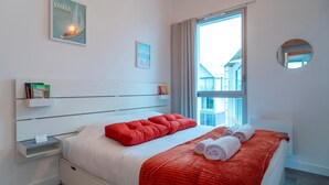 A modern hotel room with a large bed, a red blanket, and a view of a building outside.