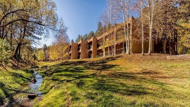 A building with multiple balconies, a grassy area, and a stream. - Cozy Creek Condo (Ruidoso)