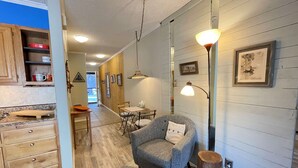 A modern kitchen with wooden cabinets, a dining area with a table and chairs, and a cozy seating area with a chair and a lamp. - Cozy Creek Condo (Ruidoso)