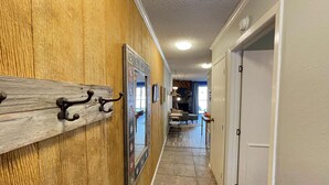 A hallway with wooden paneling, a coat rack, a mirror, and a door leading to a room. - Cozy Creek Condo (Ruidoso)