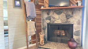 A stone fireplace with a television above it, a wooden ladder, and a vase on the mantel. - Cozy Creek Condo (Ruidoso)
