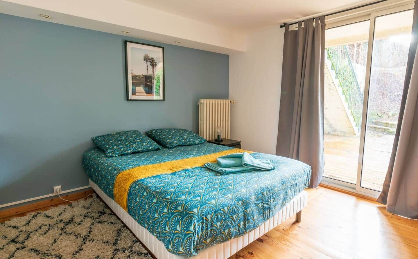 Et soveværelse med seng, et natbord, en radiator, et vindue med gardiner og et billede på væggen.