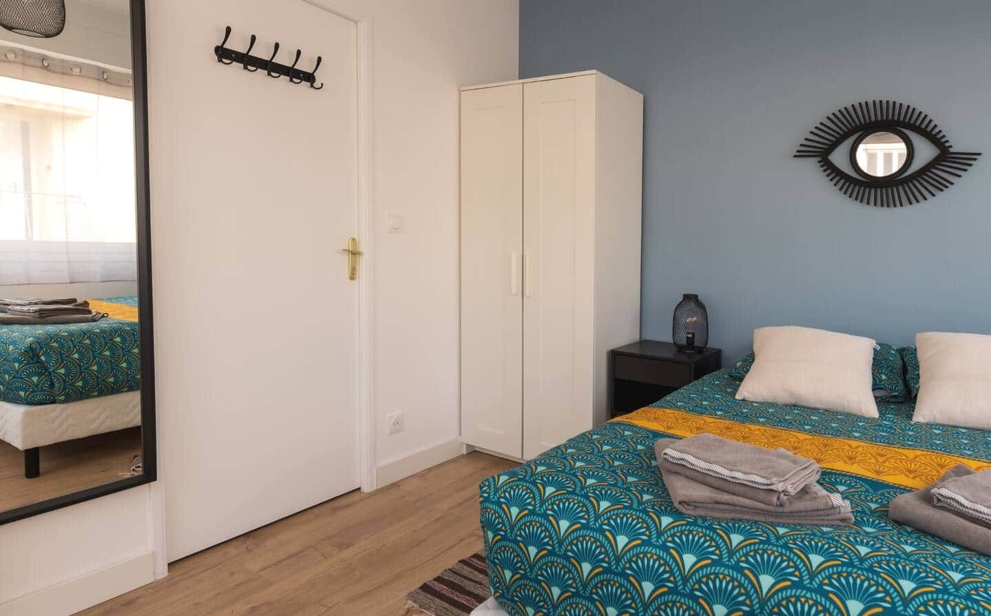 A bedroom with a bed, a wardrobe, a mirror, and a wall-mounted eye decoration.