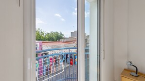Una stanza con una porta a vetri scorrevoli che dà su un balcone esterno, un comodino di legno e un corrimano in metallo.