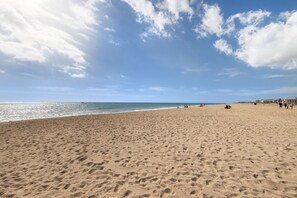 A wide sandy beach with footprints, a clear sky, and the ocean in the background.