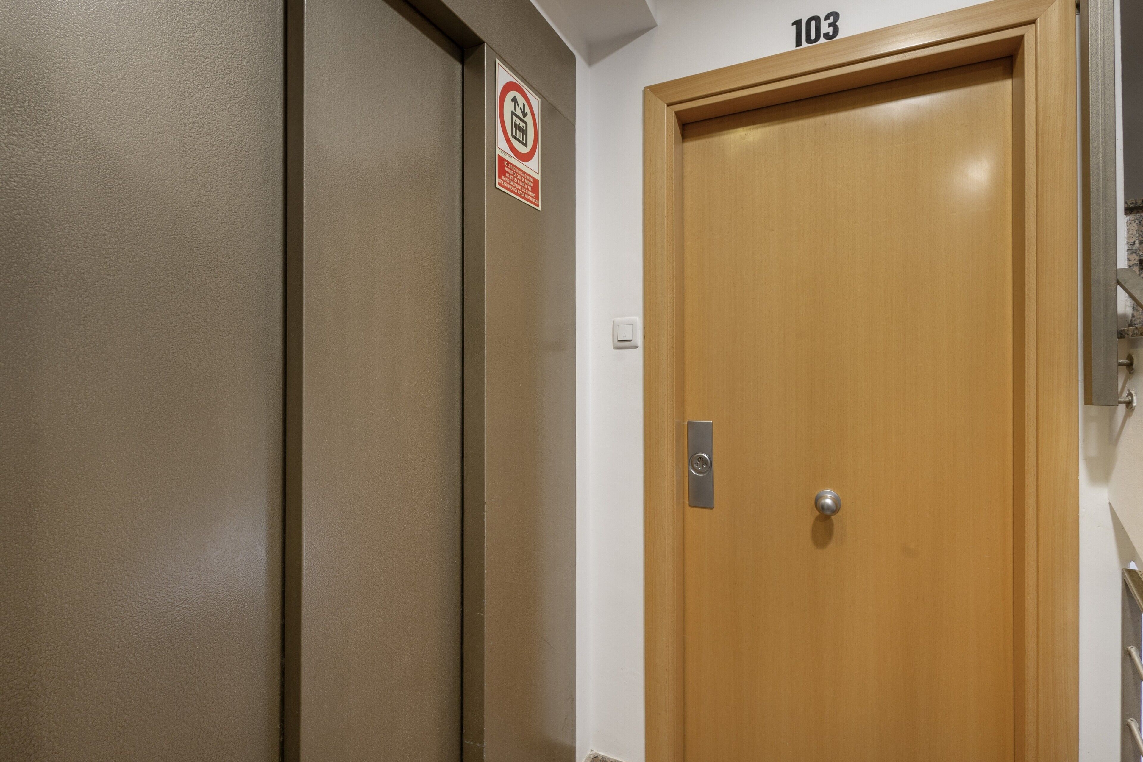 Een houten deur met het nummer 103, een rookvrij sign en een lichtschakelaar aan de muur.