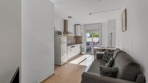 A modern kitchen with white appliances, a grey sofa, and a dining area with a table and chairs.