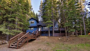 A two-story blue house with a wooden staircase leading to the front door, surrounded by tall trees.