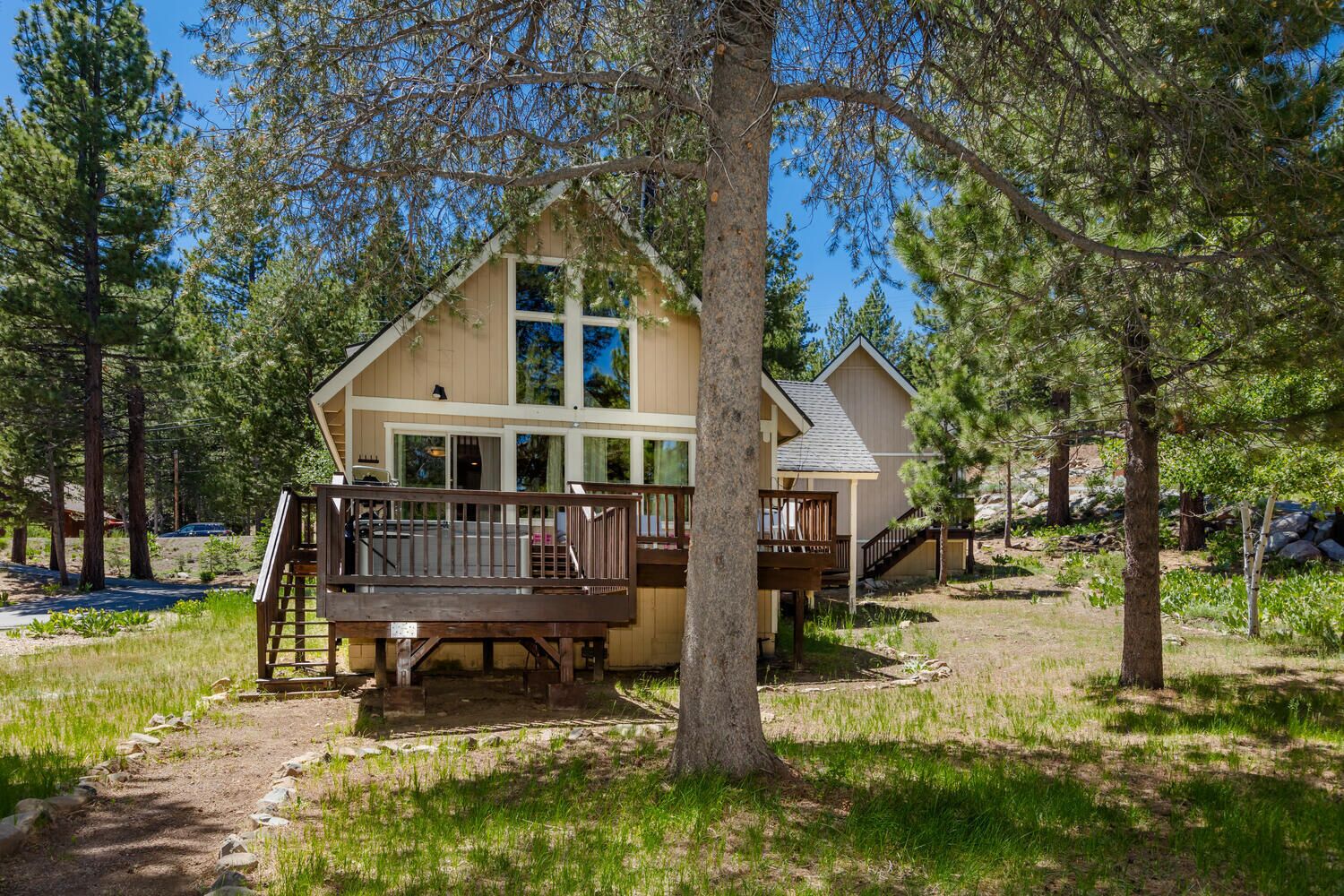 A cabin with a deck, surrounded by trees and a clear sky.