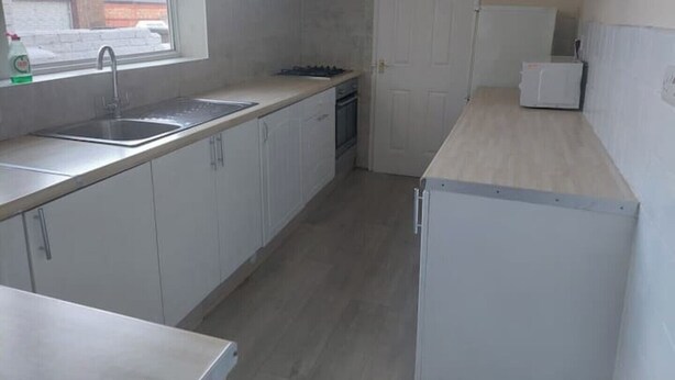 A compact kitchen with white cabinets, a stainless steel sink, a built-in oven, and a microwave. - Grace House (Stockton-on-Tees)